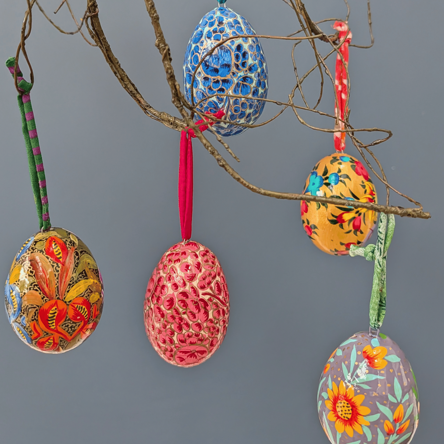 Decorative Easter eggs hanging on a branch against a gray background
