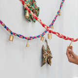 Colorful braided yarn garland with decorative bows and small gold bells on a white background.