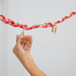 Hand holding a braided string with gold bells against a light gray background
