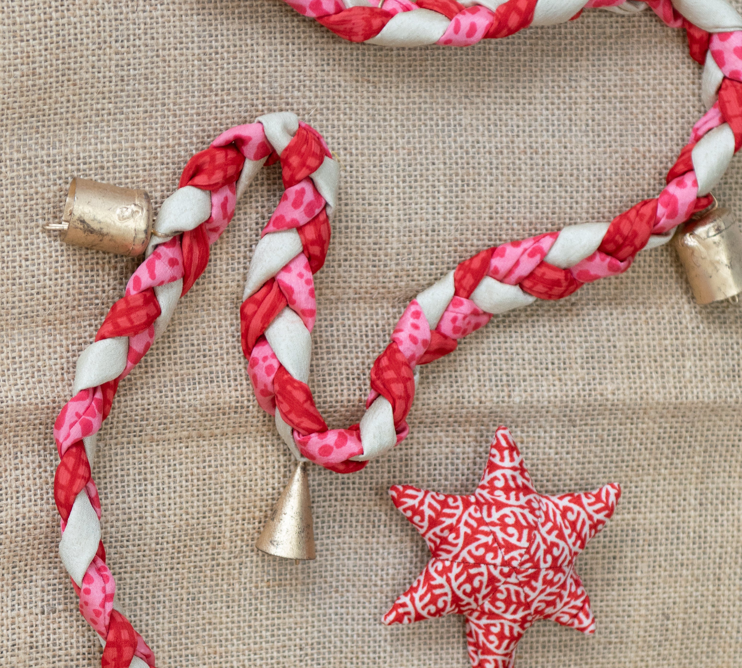 Red and white braided rope with gold bells and star-shaped decorations on a textured surface.