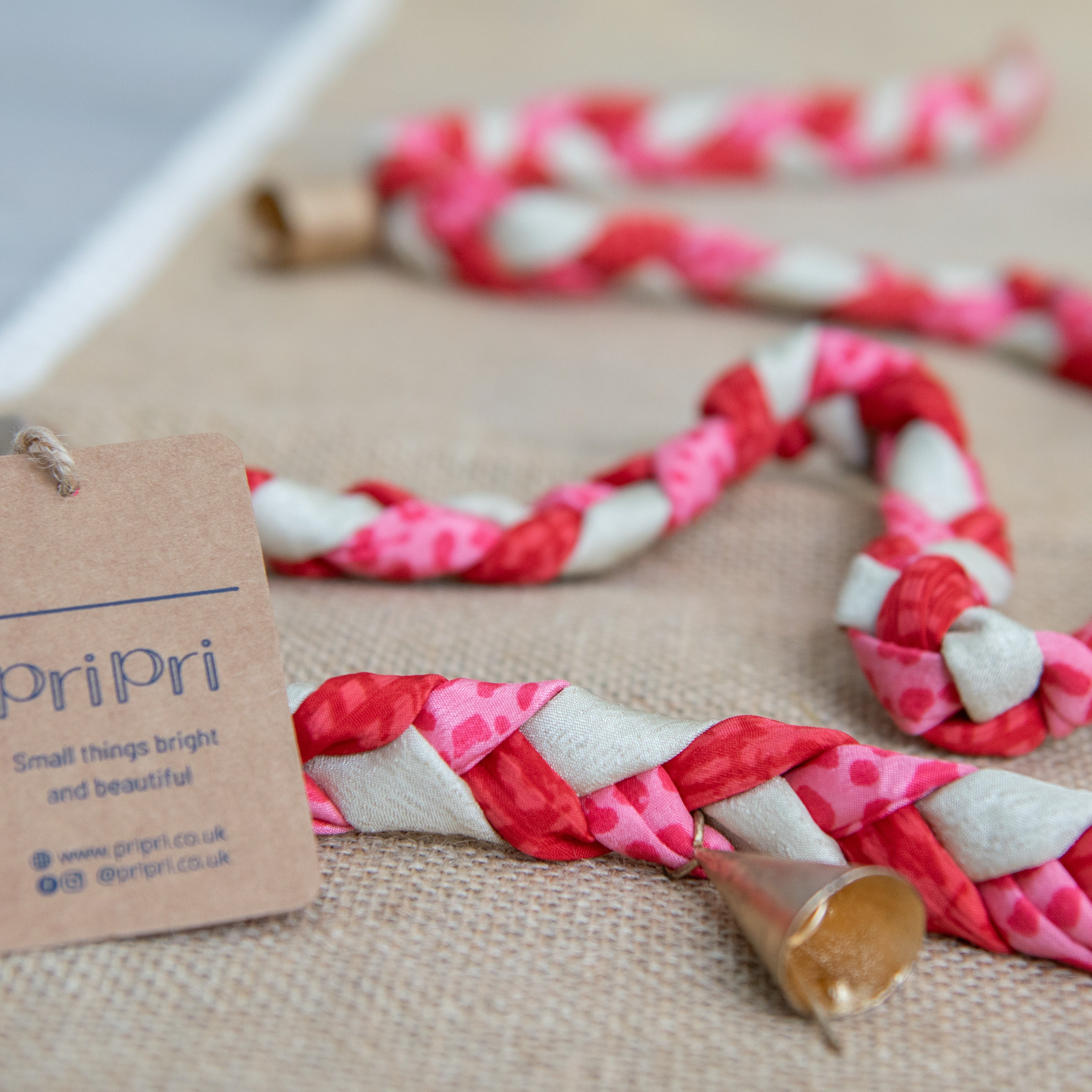 Braided garland with pink, white, and beige pattern on a textured surface with a 'PriPri' tag.