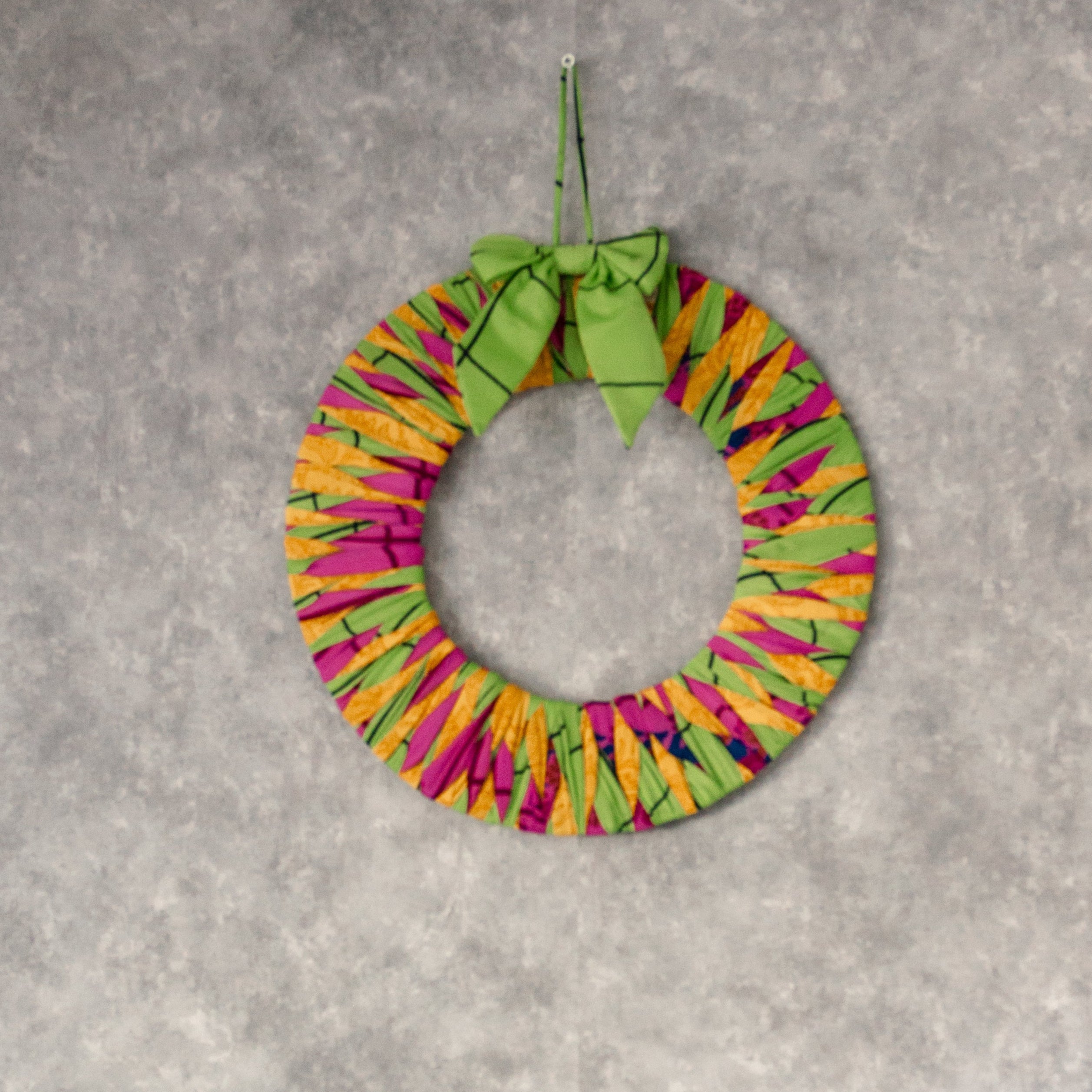 Colorful wreath and Christmas tree decoration on a gray wall with a white shelf.