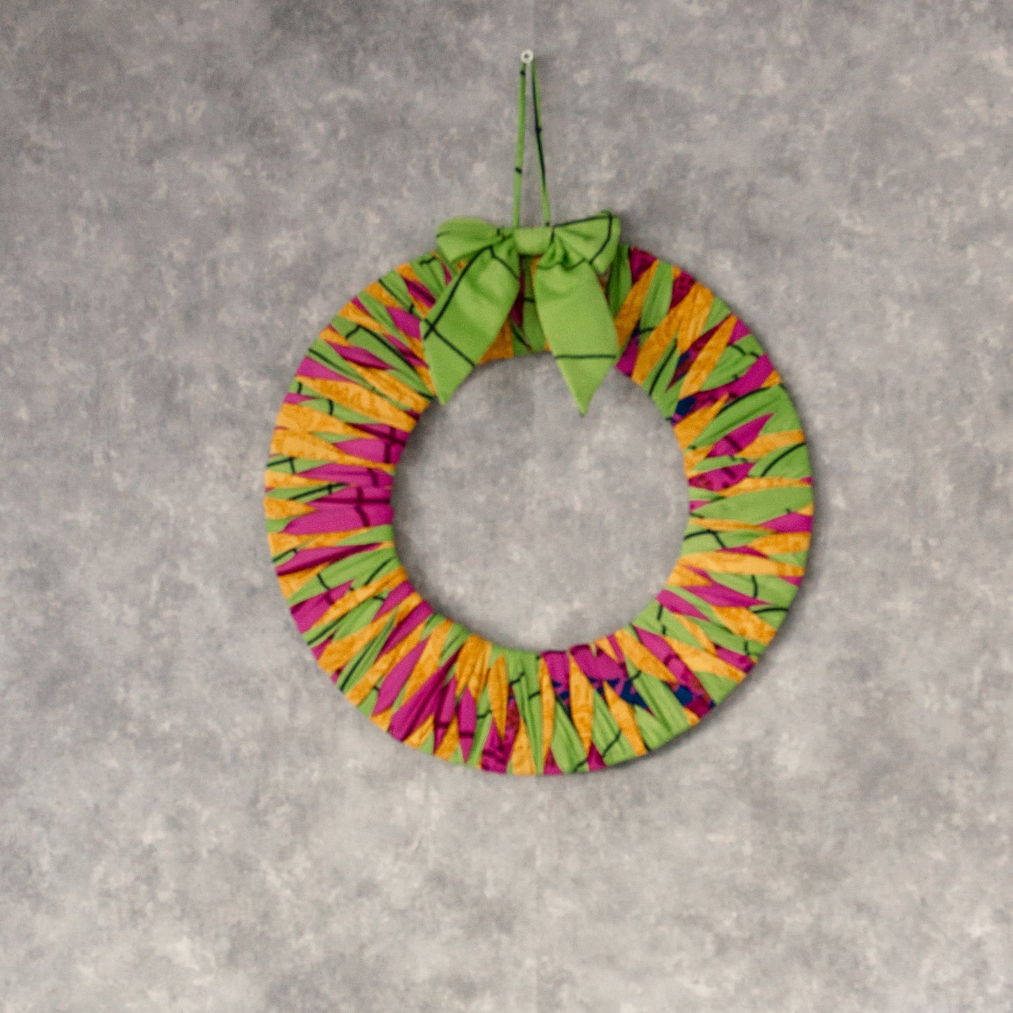 Colorful wreath and Christmas tree decoration on a gray wall with a white shelf.