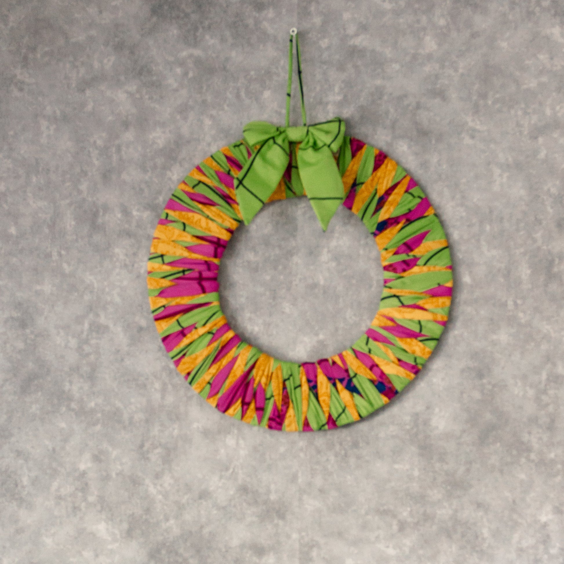 Colorful wreath and Christmas tree decoration on a gray wall with a white shelf.