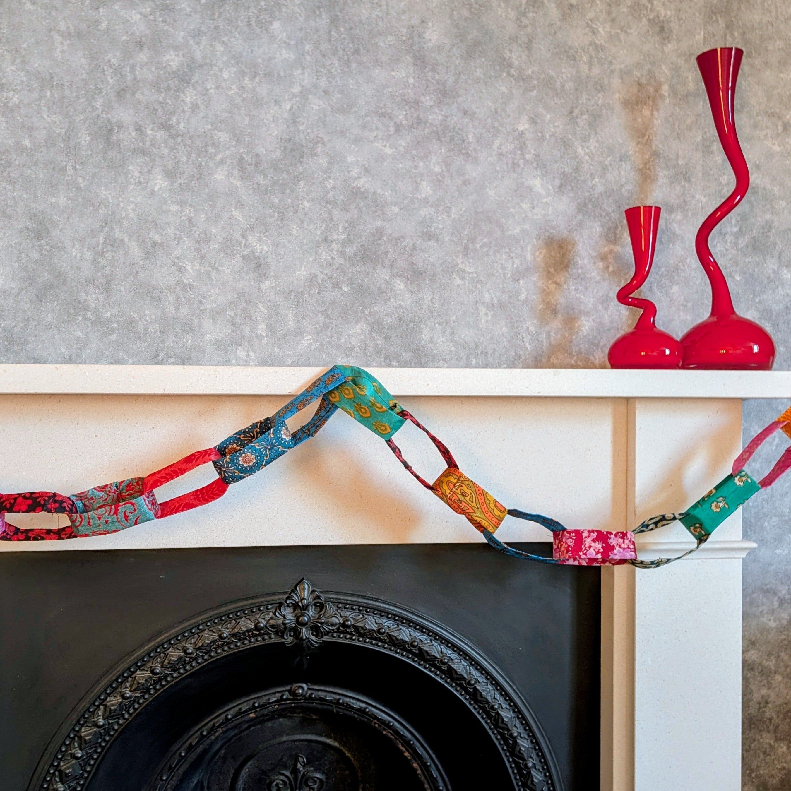 Decorative colorful fabric garland on a fireplace mantel with a textured wall background.