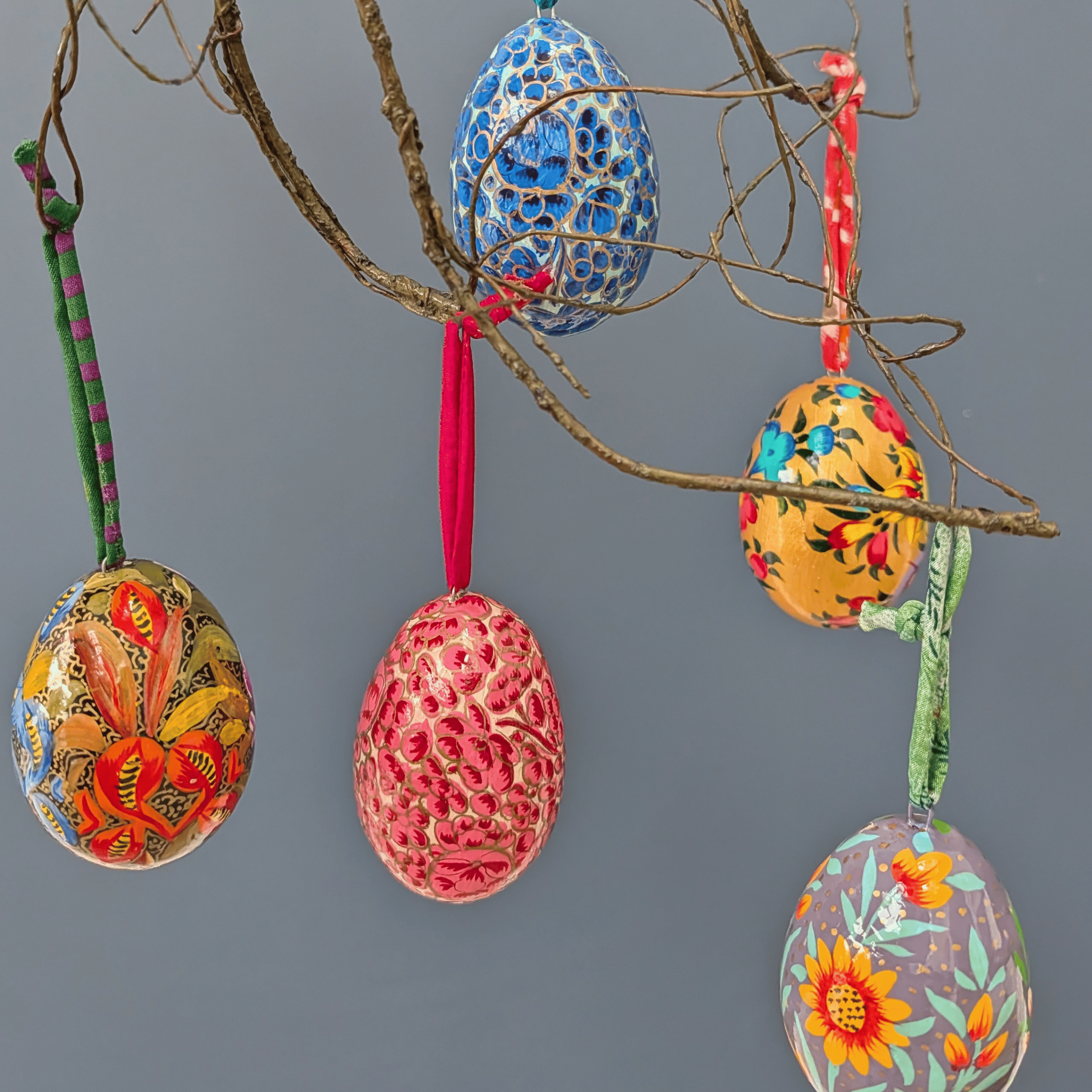 Decorative Easter eggs hanging on a branch against a gray background