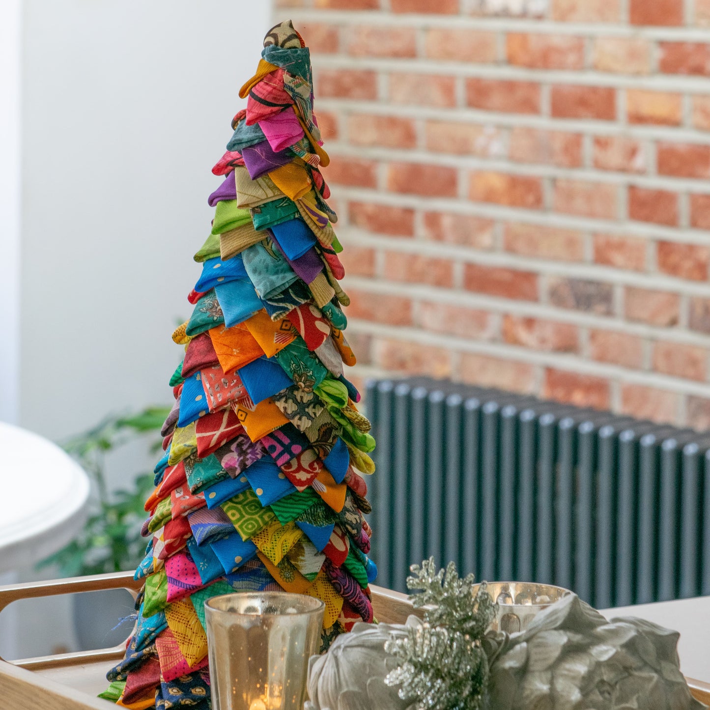 Colorful patchwork sari tree on a wooden tray with decorative items against a brick wall.