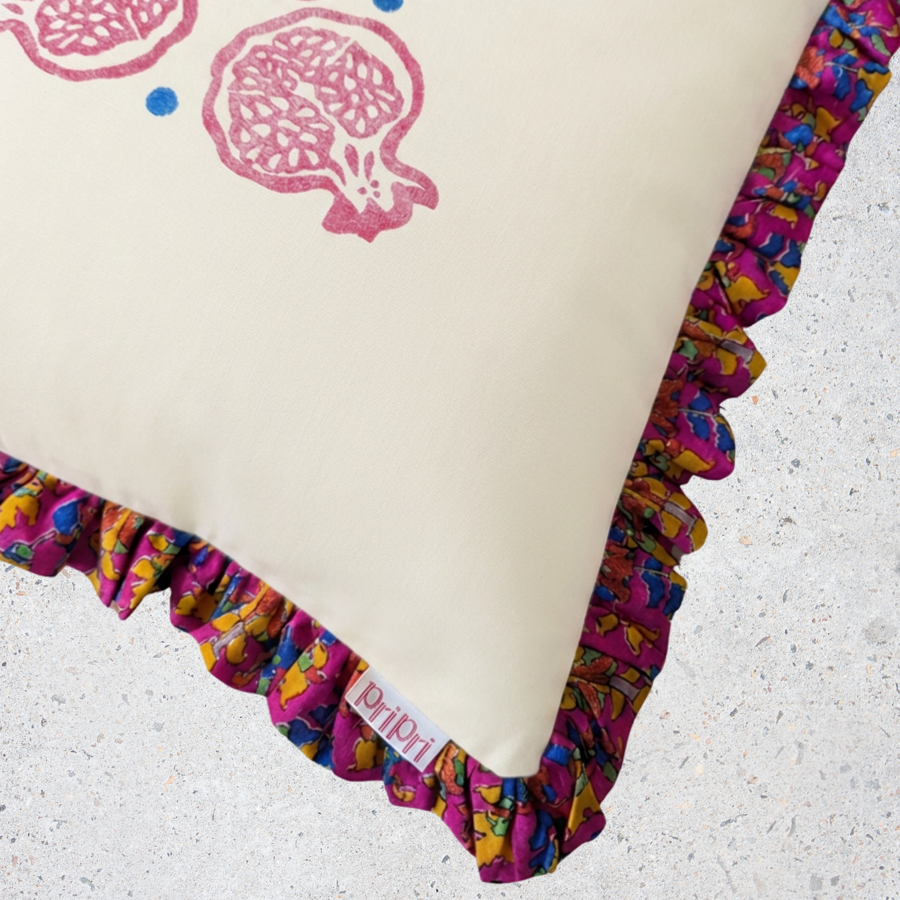 Decorative pillow with colorful ruffle trim and pomegranate pattern on a textured surface