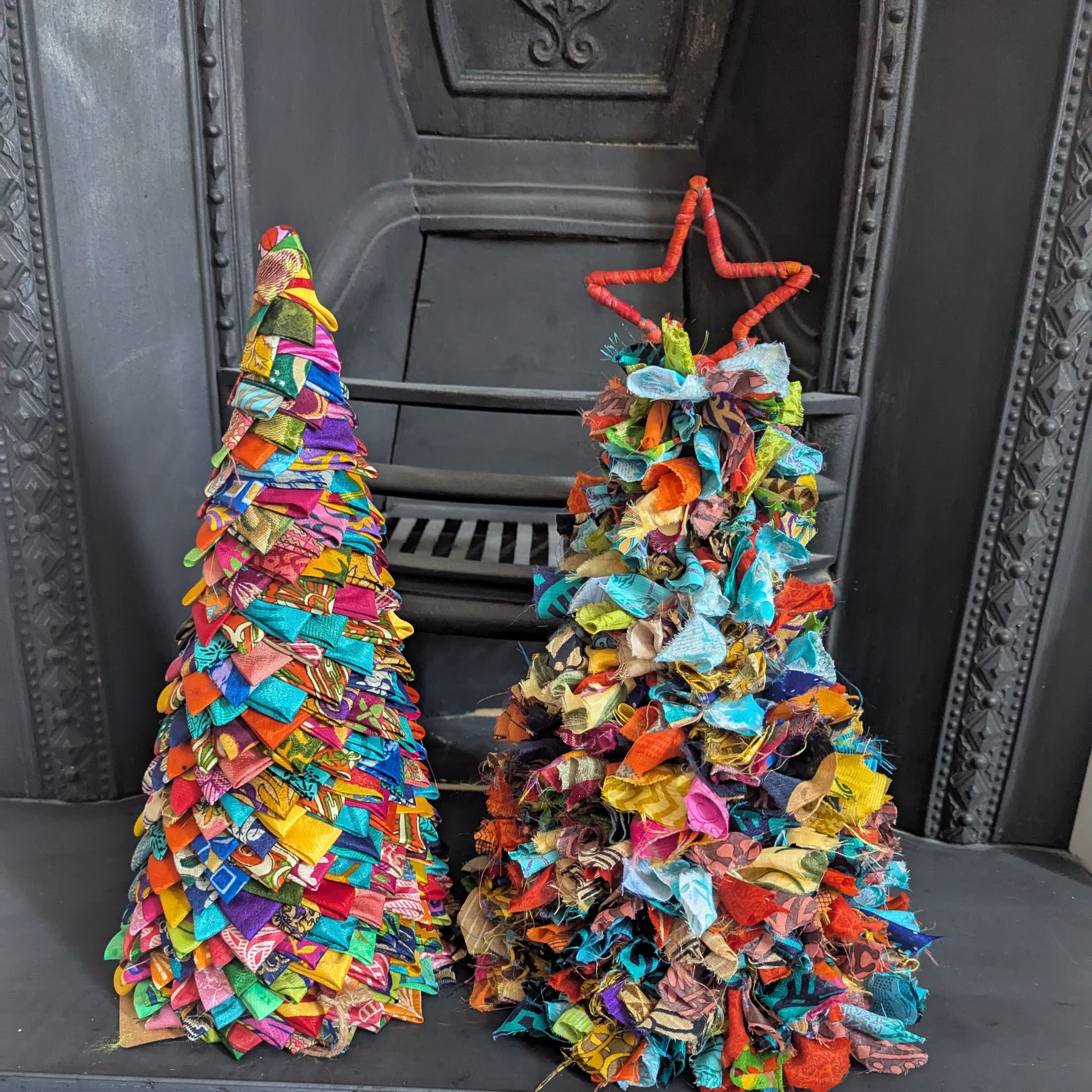 Two colorful fabric Christmas trees in front of a fireplace.