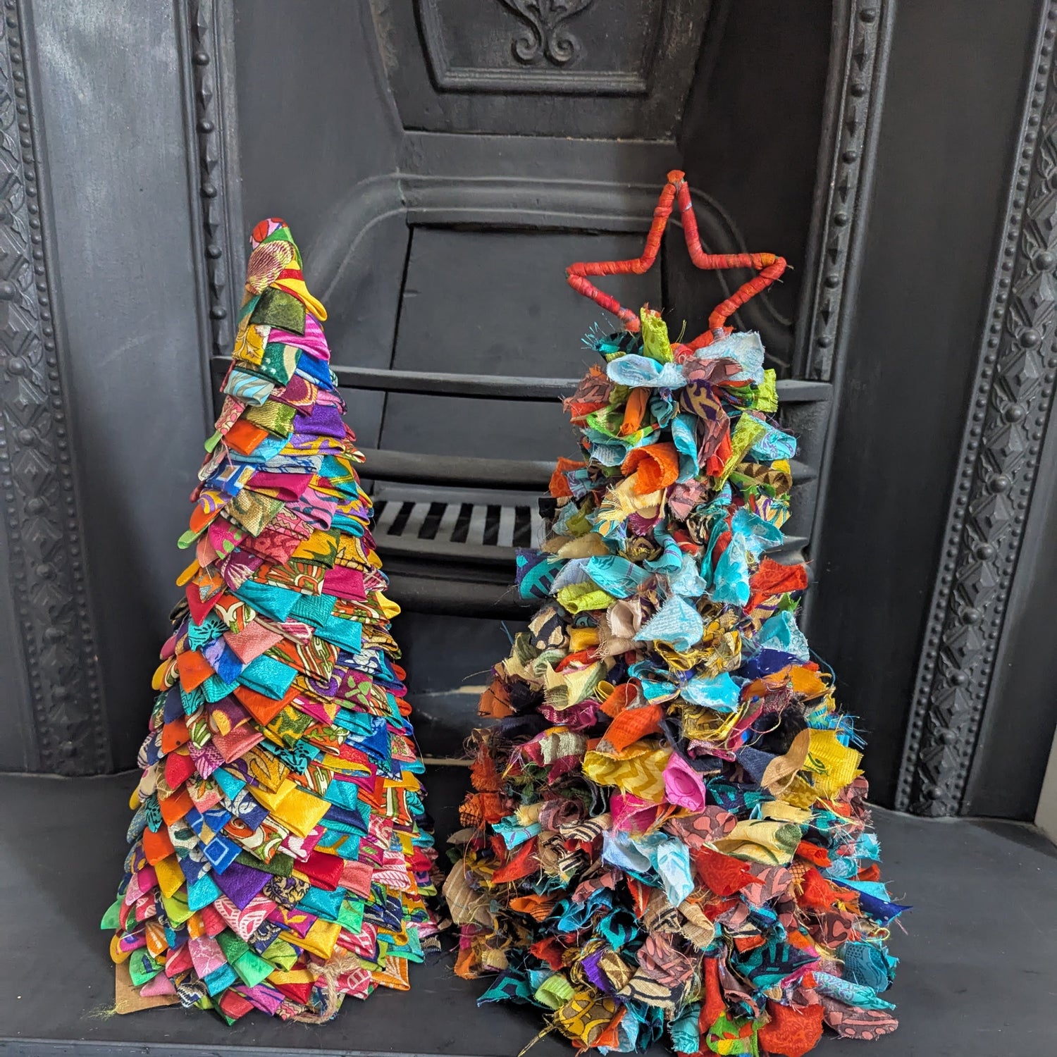 Two colorful fabric Christmas trees in front of a fireplace.