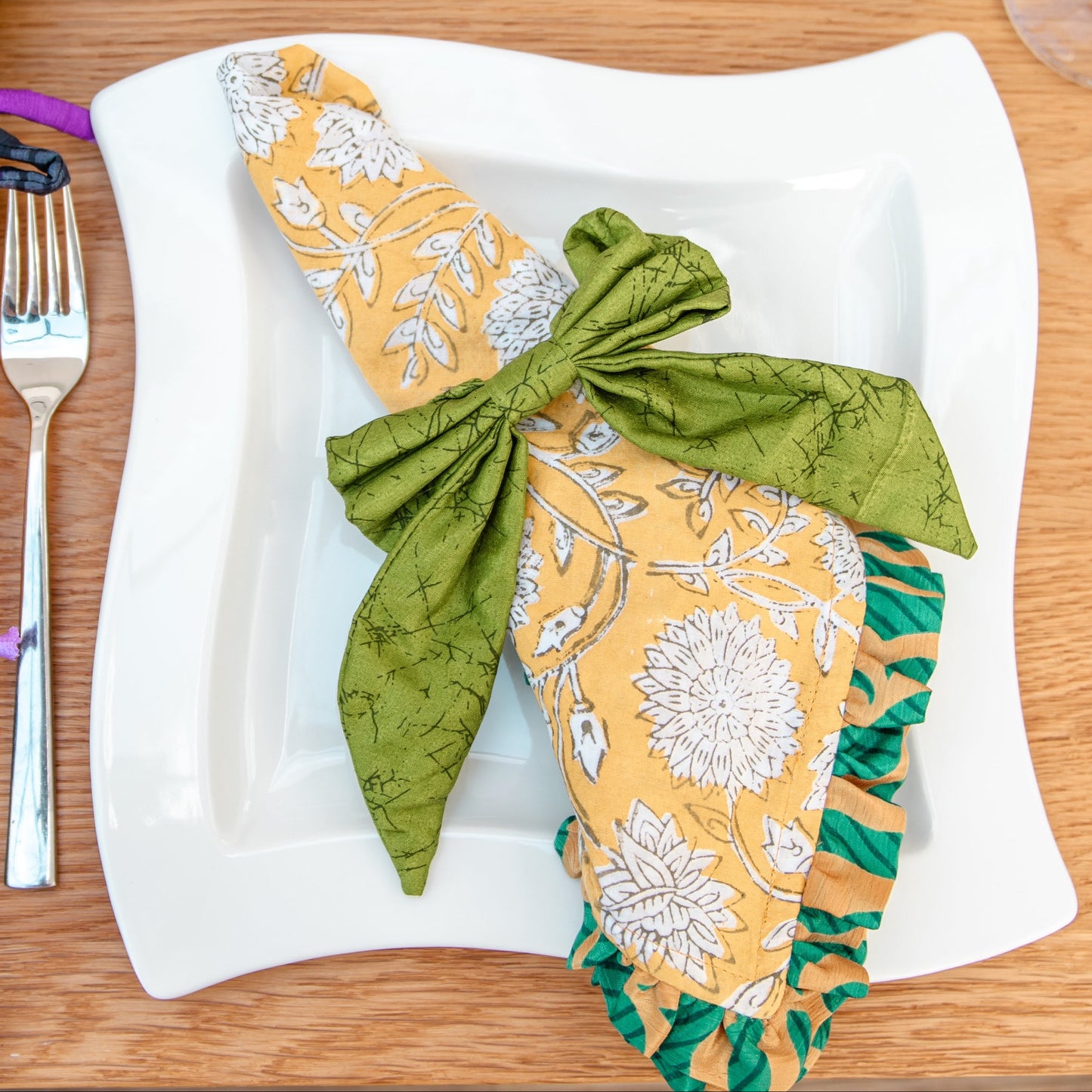 Decorative napkins tied with ribbons on a wooden table setting with cutlery and candles.