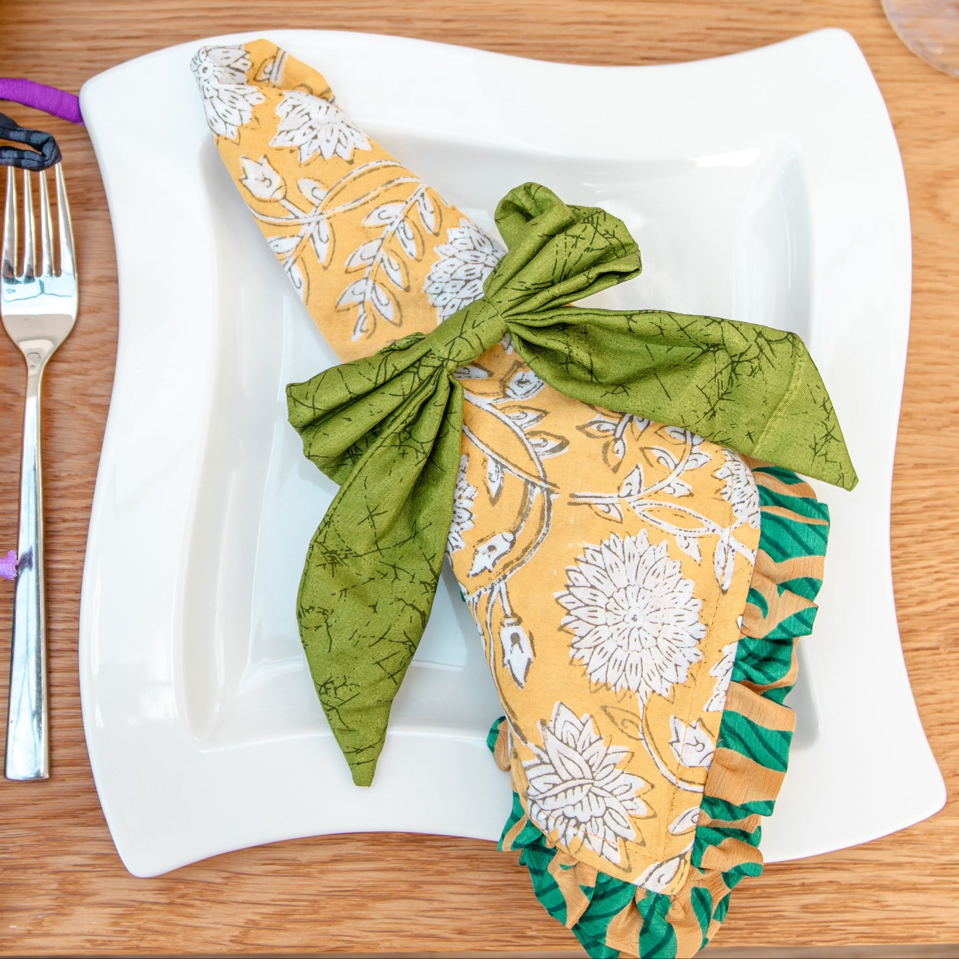 Decorative napkins tied with ribbons on a wooden table setting with cutlery and candles.