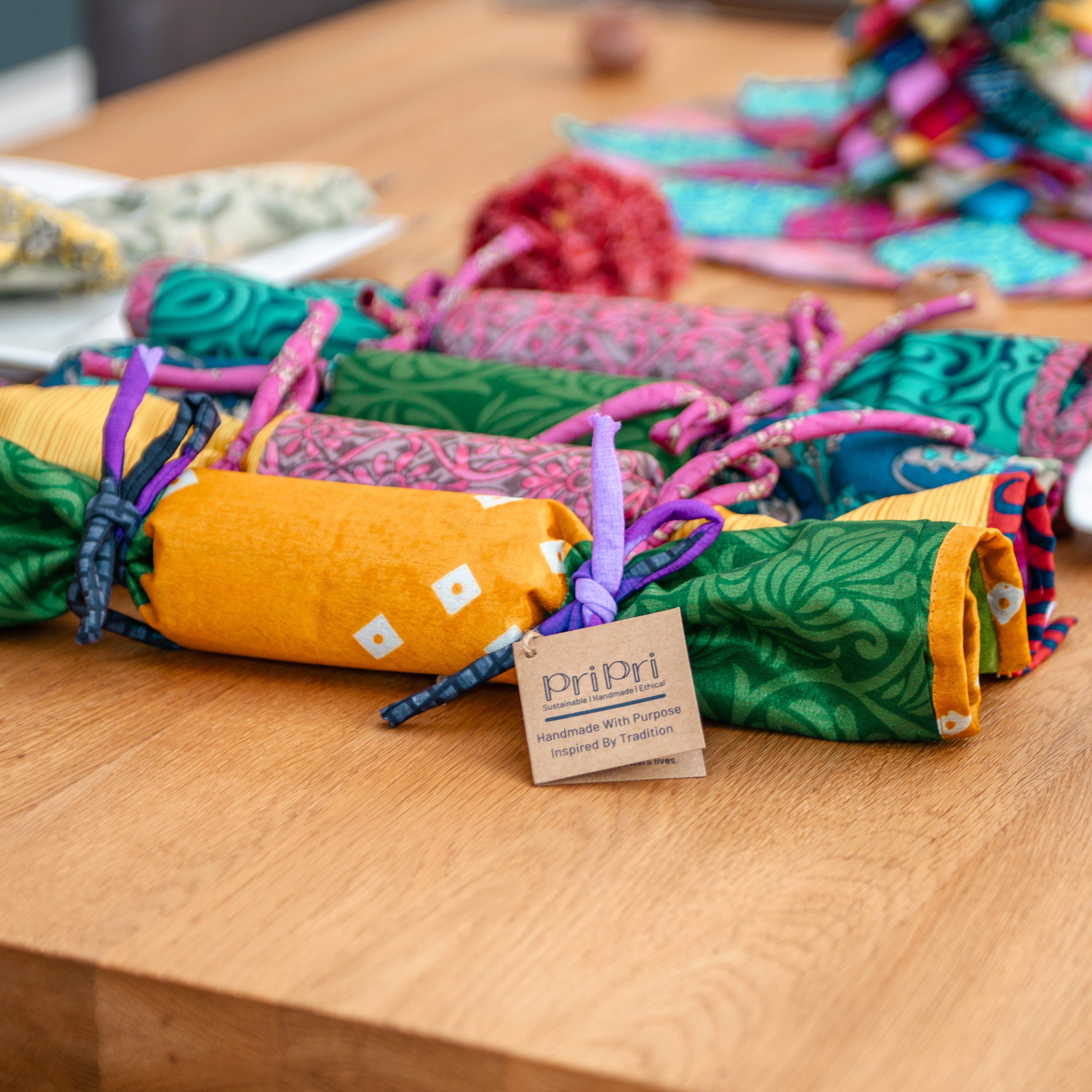 Colorful fabric crackers on a wooden table with a Pri Pri swing tag