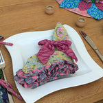 Decorative table setting with colorful napkins and a small tree on a wooden table.
