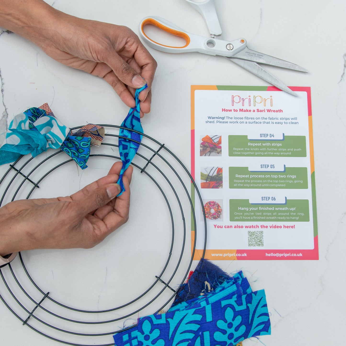 Person making a craft project with blue fabric and scissors on a white marble surface.