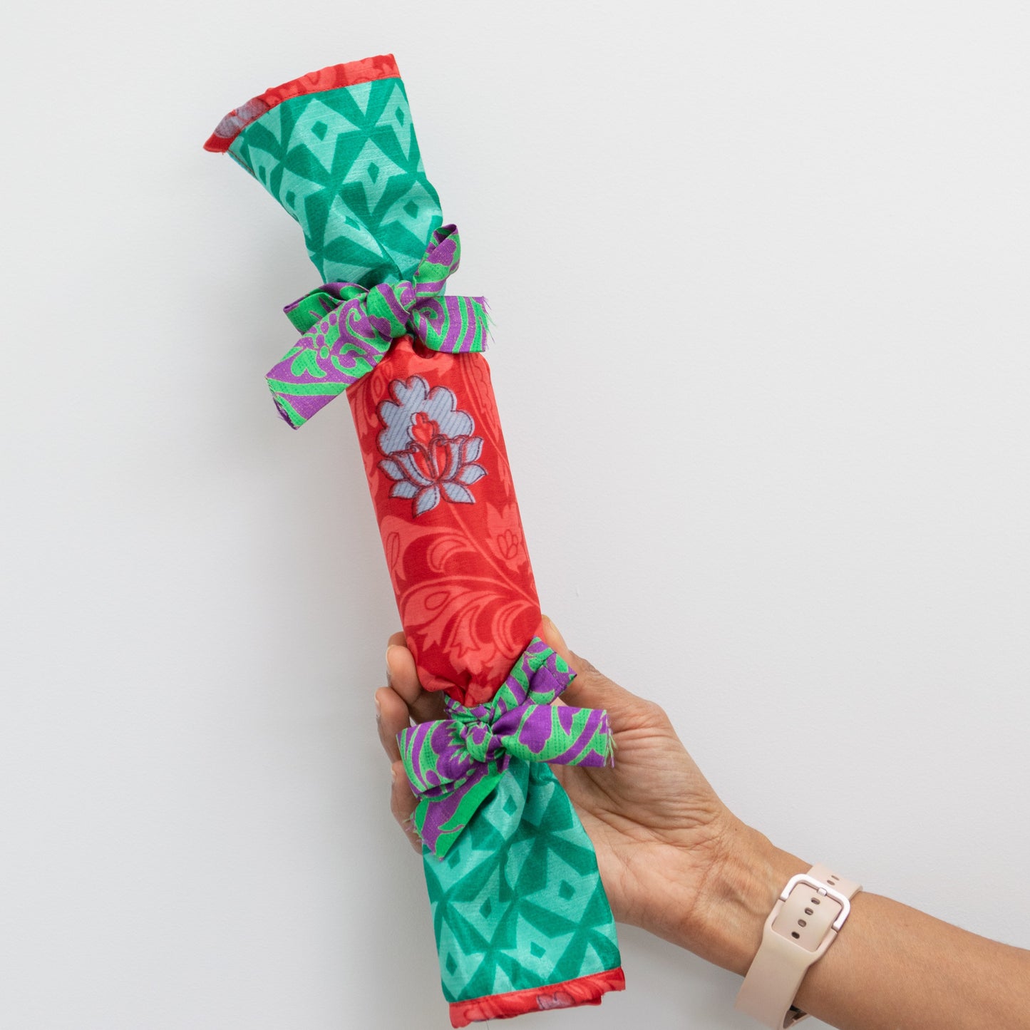 Colorful cracker wrapped in patterned fabric held by a hand on a white background