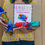 Person holding a box of 'Pri Pri' reusable cracker set with colorful cracker packages.