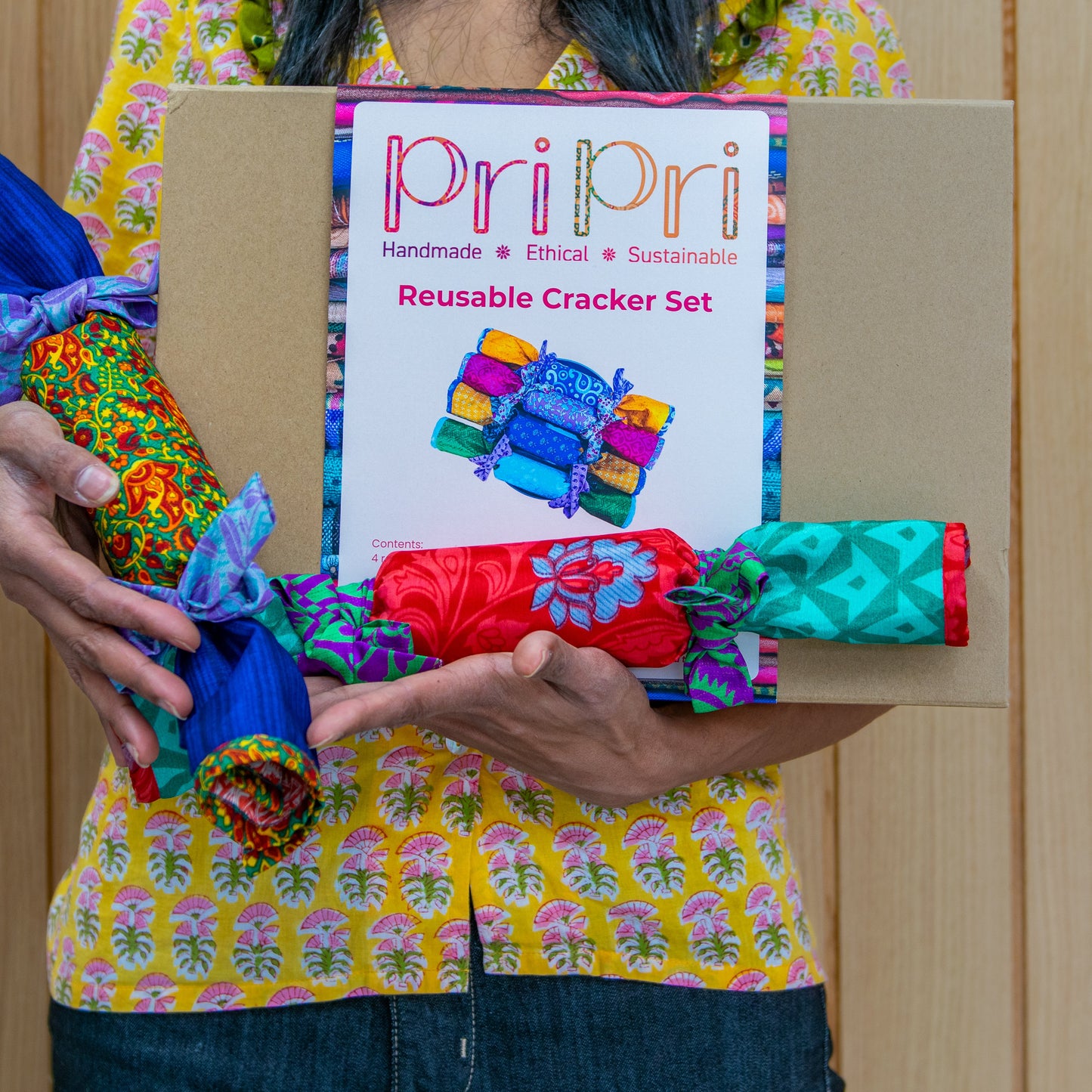 Person holding a box of 'Pri Pri' reusable cracker set with colorful cracker packages.