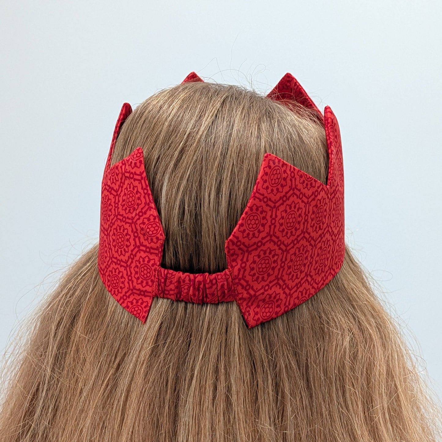 Red sari crown on a person with light brown hair against a light background
