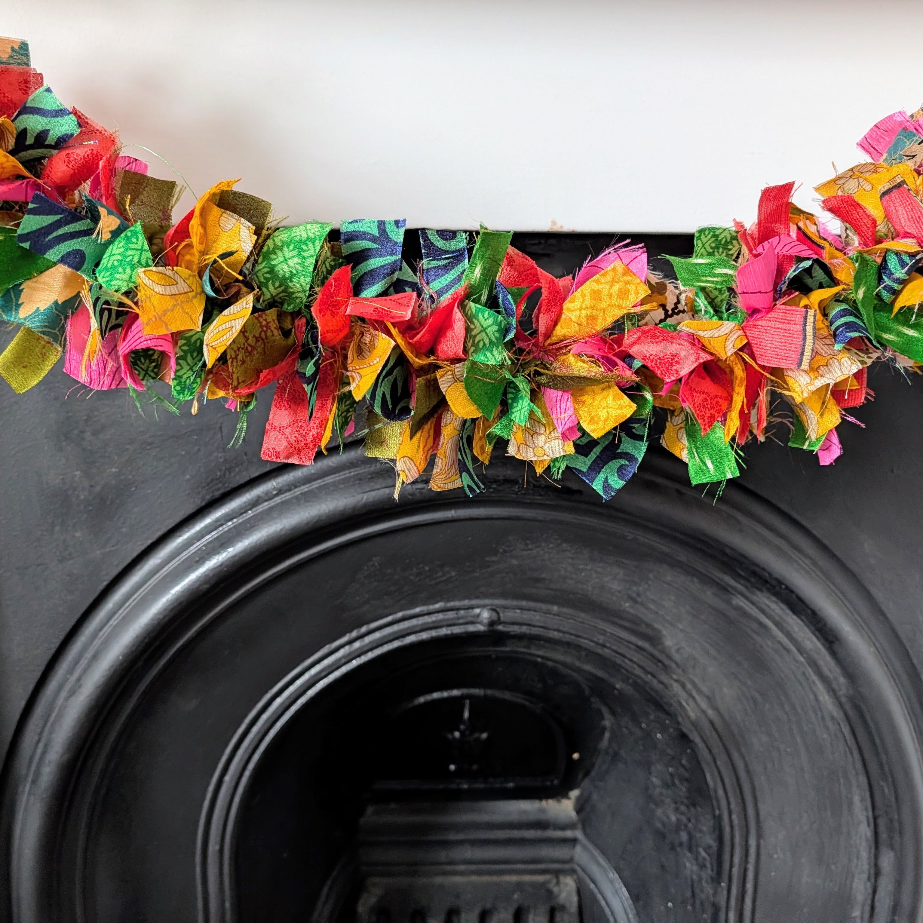Colorful fabric garland draped over a black fireplace.